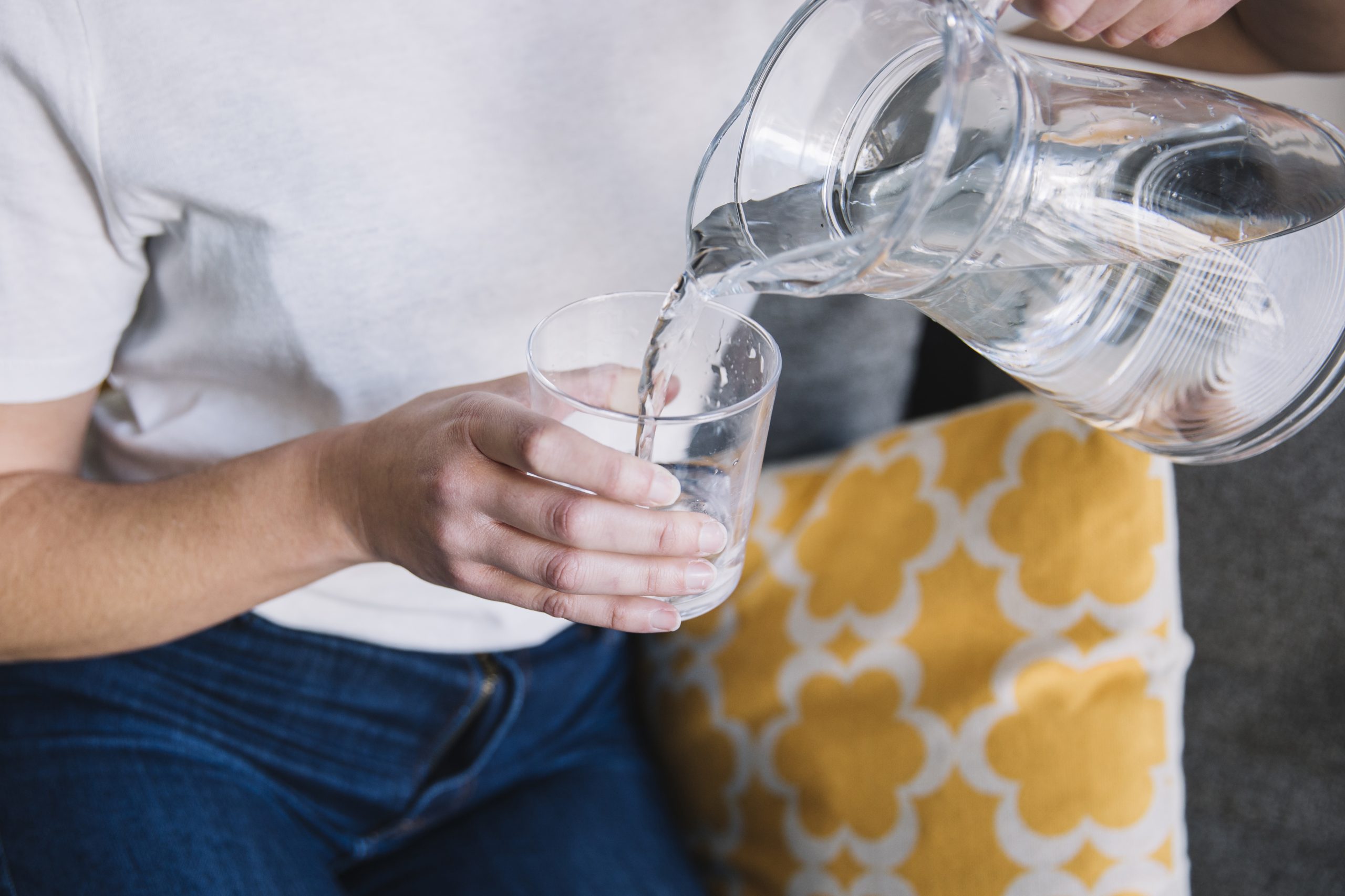 crop-woman-sofa-pouring-water